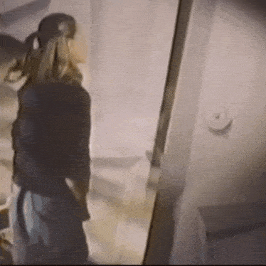 a woman is standing in front of a door and looking at herself in a mirror