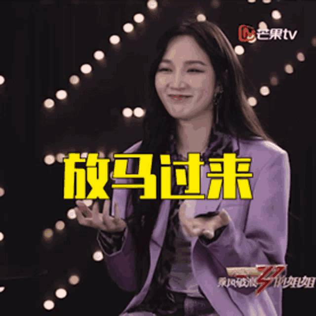 a woman in a purple jacket is smiling in front of a tv logo