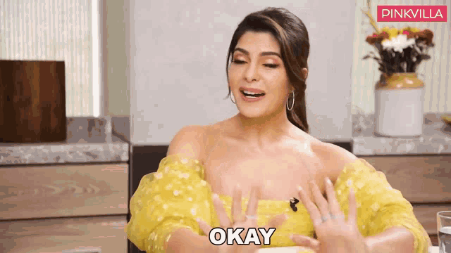 a woman in a yellow dress says okay in front of a pinkvilla banner