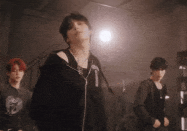 a group of young men are standing in a dark room and one of them is wearing a black hoodie