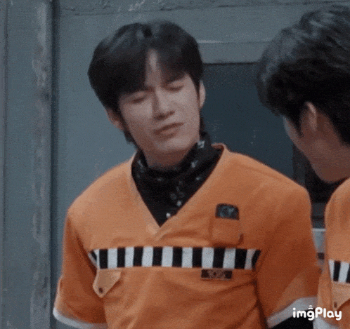 a man wearing an orange shirt with a black and white striped pattern is talking to another man .