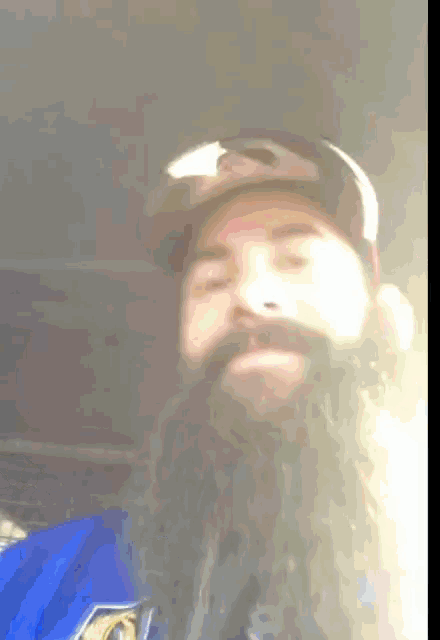 a man with a beard wears a hat and a blue shirt