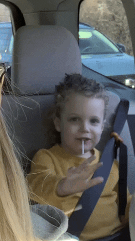 a little boy in a car seat eating a lollipop