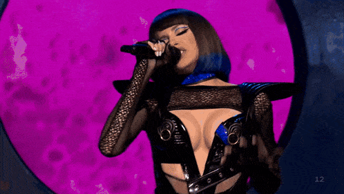 a woman singing into a microphone in front of a purple background with the number 12