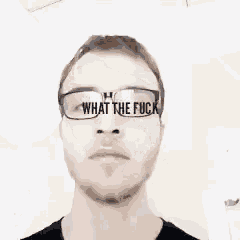 a man with glasses is laying on his back with the words `` what the fuck '' written on the bottom of his face .