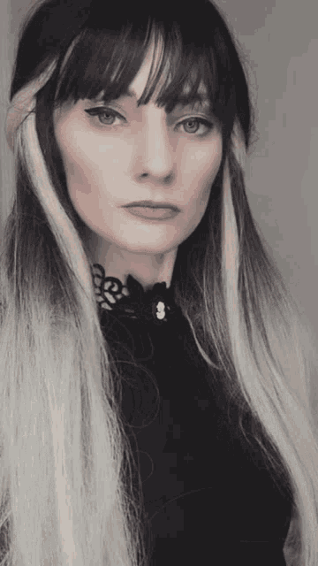 a woman with long black hair and white streaks is wearing a black shirt