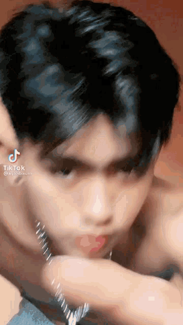 a young man with a necklace around his neck is licking his lips .