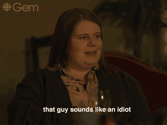 a woman is sitting at a table with a glass of wine and says " that guy sounds like an idiot "