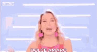 a woman in a pink dress and pink earrings is smiling and giving the middle finger .