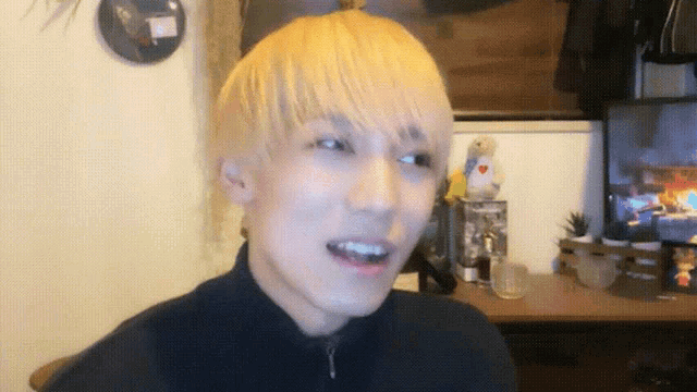 a young man with blonde hair is smiling in front of a clock that says ' clock ' on it