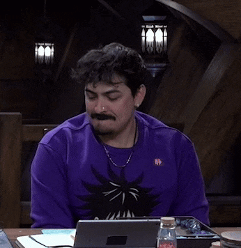a man wearing a purple sweater is sitting at a table with a laptop and a bottle of water .