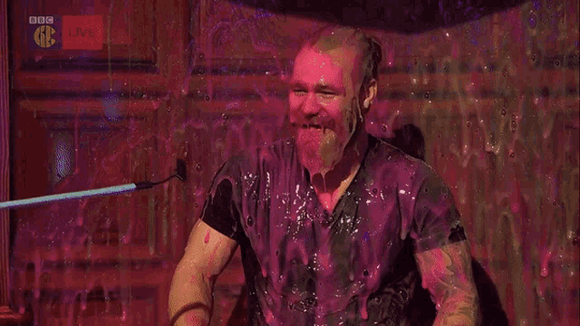 a man is covered in pink liquid in front of a bbc live sign