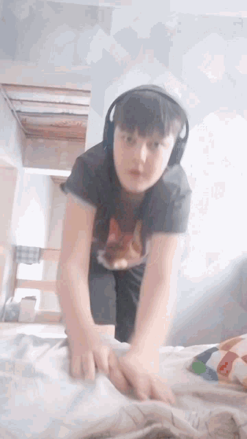 a boy wearing headphones and a shirt with a cat on it is standing on a bed
