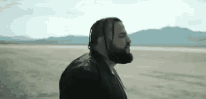 a man with a beard and braids is standing in a desert .