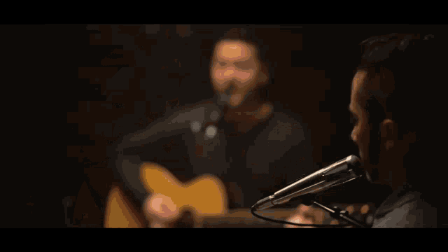 a man singing into a microphone while another man plays guitar