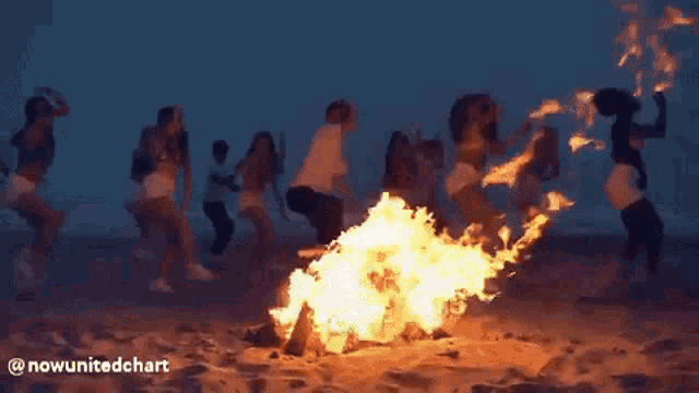 a group of women are dancing around a campfire on the beach .