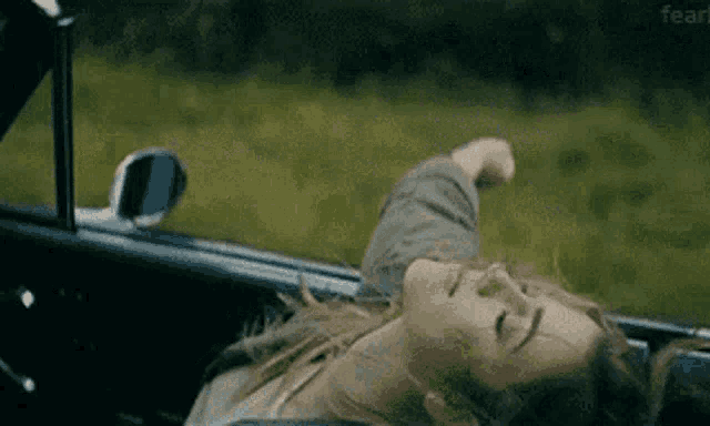 a woman is laying in the back of a car with her arms out the window .