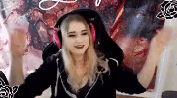 a woman wearing headphones and a black hoodie is dancing in front of a wall with a picture of a sword .