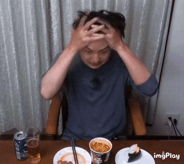 a man is sitting at a table with a can of soda and a cup of noodles