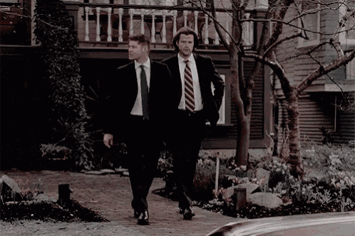 two men in suits and ties are walking down a sidewalk next to a house .