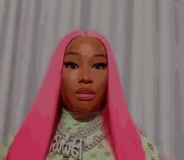 a woman with long pink hair is wearing a necklace and giving a middle finger .