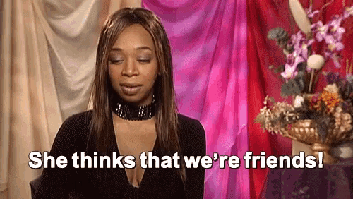a woman is sitting in front of a pink curtain and flowers and says `` she thinks that we 're friends ''