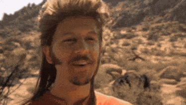 a man with a mullet and a beard smiles in the desert