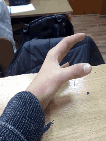 a person 's hand is resting on a wooden table with a backpack in the background