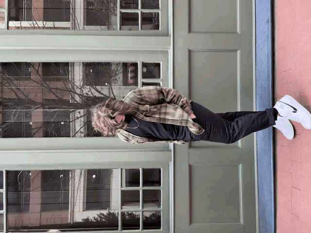 a person wearing a plaid shirt and white nike shoes stands in front of a door