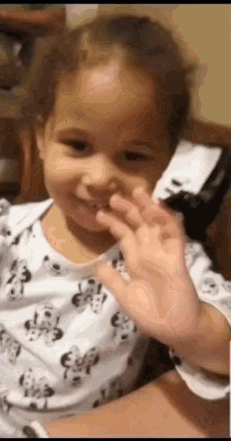 a little girl wearing a dalmatian print shirt is waving her hand