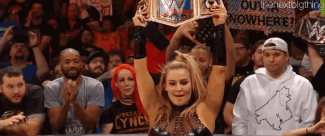 a woman is holding up a wrestling championship while a crowd applauds