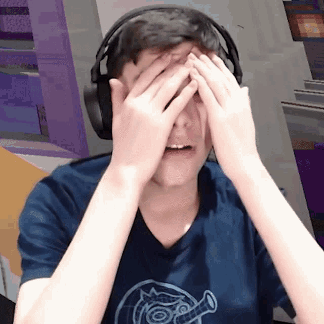 a young man wearing headphones covering his face with his hands
