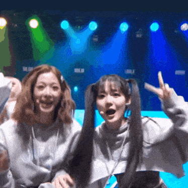two girls are posing for a picture in front of a stage with a blue light behind them