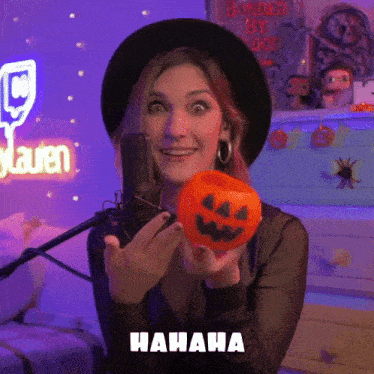 a woman in a black hat is holding a pumpkin in front of a microphone with the word hahaha above her