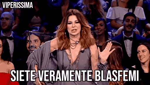 a woman in a gray dress is standing in front of a crowd of people and saying siete veramente blasfemi .