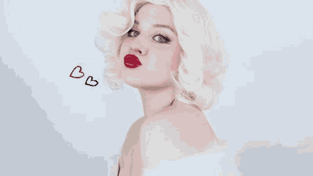 a woman in a blonde wig blowing a kiss with hearts drawn on the wall behind her .