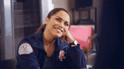 a woman in a firefighter 's uniform is smiling with her hand on her chin .