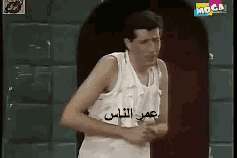 a man in a white tank top is standing in front of a door with arabic writing on it .