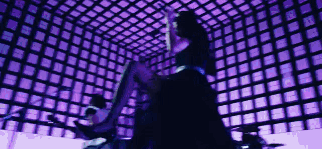 a man is playing a guitar in a purple room with a lot of squares on the wall .