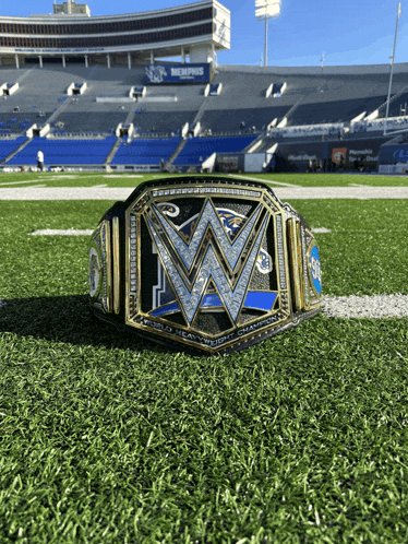 a wrestler 's belt sits on a football field with a stadium in the background