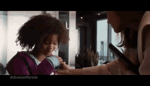 a girl with curly hair is being held by a woman in a room with the hashtag anniemovie on the bottom