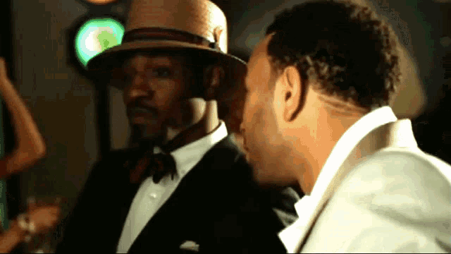 a man wearing a straw hat is talking to another man in a suit