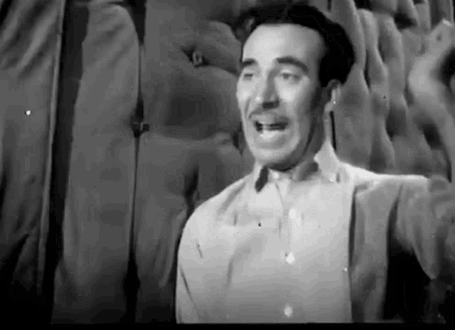 a man in a white shirt and suspenders is standing in front of a wall .