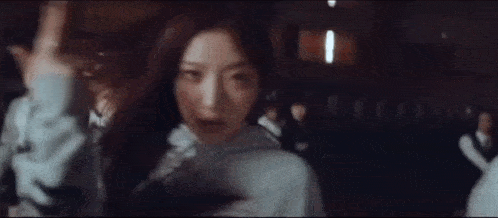 a woman is standing in front of a group of people in a dark room and looking at the camera .