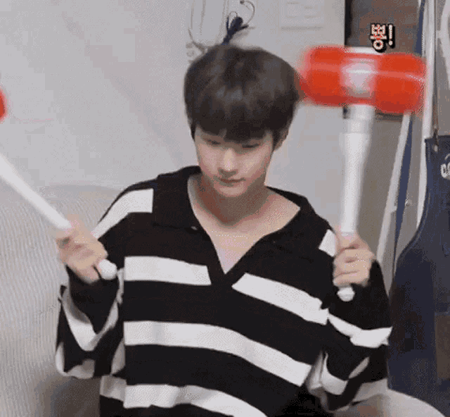 a man in a striped sweater is holding a red hammer over his head .