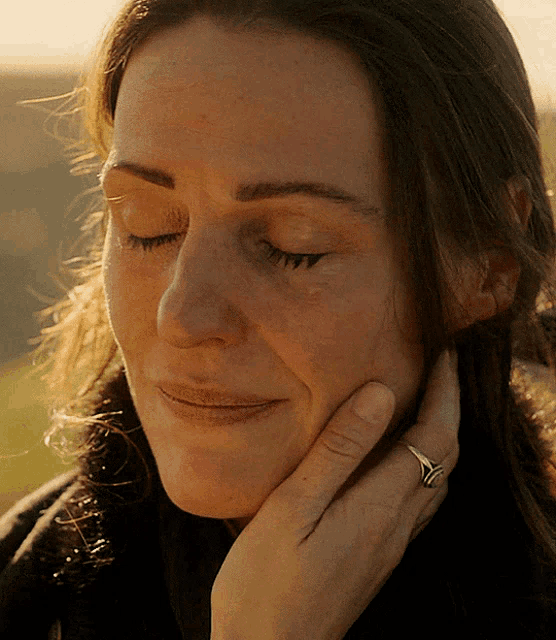 a close up of a woman 's face with her eyes closed and a ring on her finger