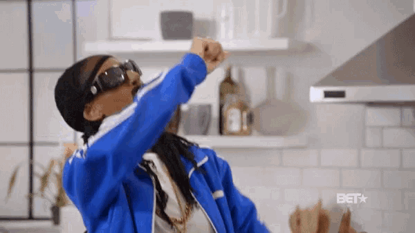 a woman in a blue jacket and sunglasses is standing in a kitchen .