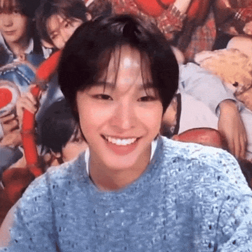 a young man in a blue sweater is smiling in front of a crowd of people .
