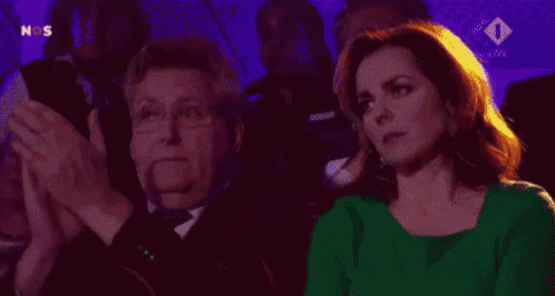 a woman in a green shirt sits next to a man in a suit and tie in a dark room