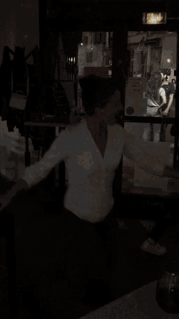 a woman in a white shirt sits at a table in the dark